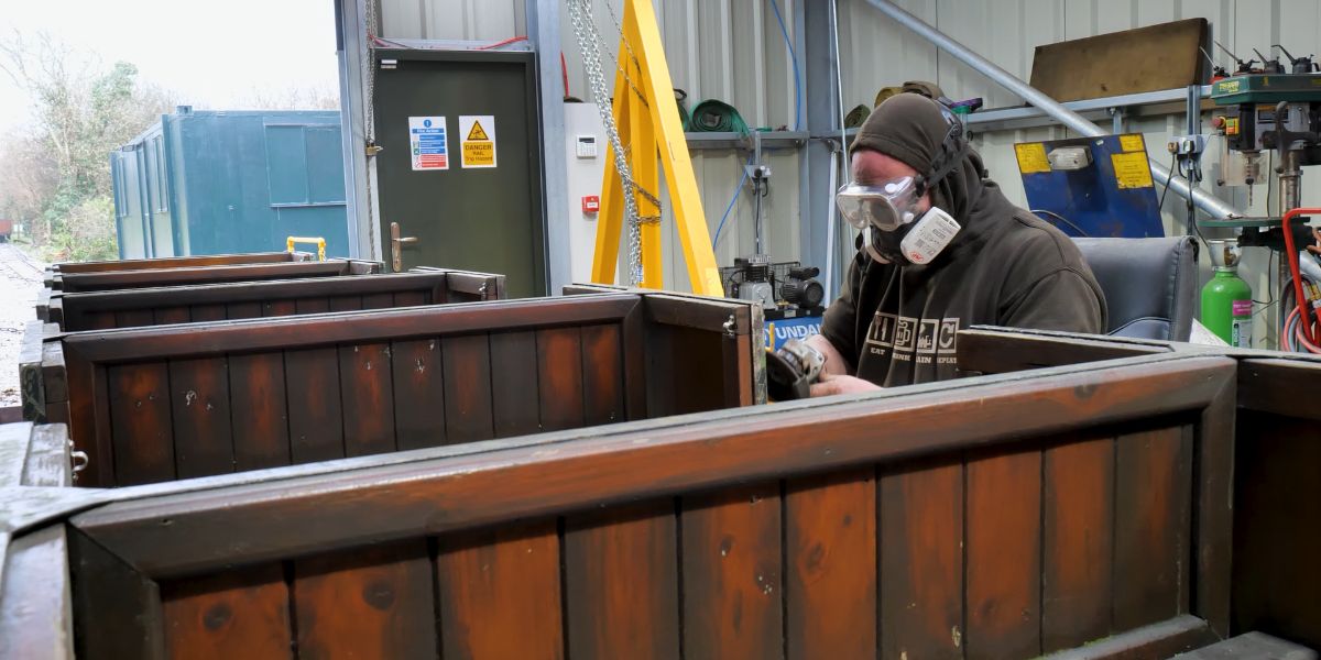A member of the Lappa Valley team works sanding down the paintwork on open top carriage L3